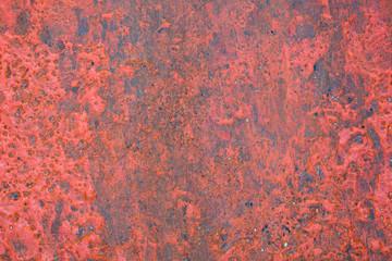 old gray concrete wall with protruding stones and peeling bright red paint. rough surface texture