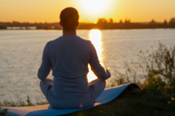 A young man sits on a lake at sunset, doing yoga. Sits in the pose of ardhapadmasana, padmasana. Balance, harmony, balance, concentration, relaxation.