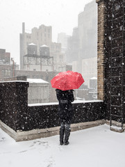Woman standing alone on rooftop with red umbrella in falling snow