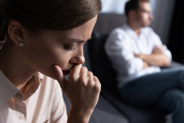 upset pensive young woman and husband sitting on sofa