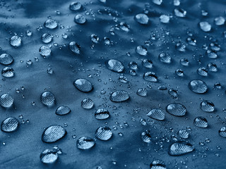 Rain water droplets on blue fiber waterproof fabric. Blue background.