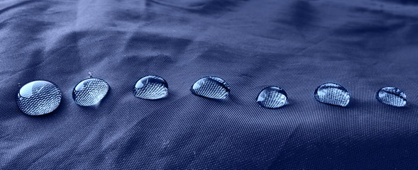 Rain water droplets on blue fiber waterproof fabric. Blue background.