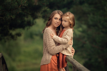 young mother hugging her daughter sitting on the wooden railing in the forest
