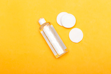 Makeup remove skin care. Tonic for face skin or makeup remover in a plastic bottle, cotton pads and wooden cotton buds on yellow background. Hygiene supplies, beauty tools and skin