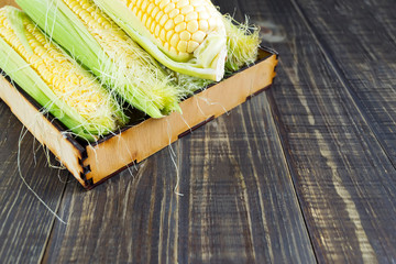 Fresh corn with green leaves on a dark wooden table. Healthy vegetable