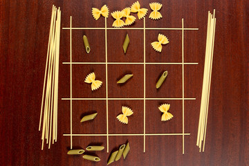 Italian pasta. Tic Tac Toe or Xs and Os game made from raw spaghetti, yellow farfalle and green...