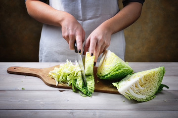 Woman cutting savoy cabbage on wood background