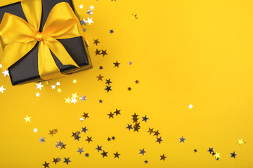 Gift box on yellow background with sparkling confetti.