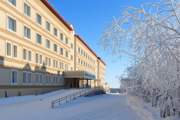 Winter view of the hospital building. Snowy street and snow-covered branches of bushes. Cold frosty weather. Location place: city of Anadyr, Chukotka, Siberia, Far East of Russia.
