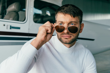 pensive man in sunglasses looking away near plane