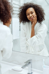 Skin care. Woman touching face, looking at mirror at bathroom