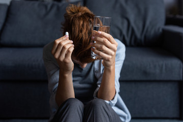 sick woman holding pill and glass of water at home