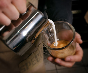 Barista makes latte coffee with milk in cafe closeup