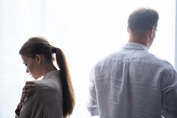 back view of upset woman and man in shirts standing near window