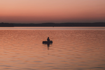 Naklejka premium silhouette of fishermen alone in a boat swimming on a lake. sunset background.