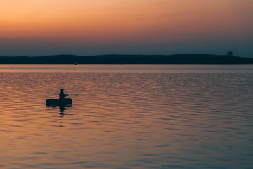 silhouette of fishermen alone in a boat swimming on a lake. sunset background.