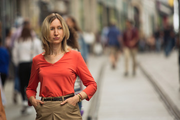 Blond woman in a red blouse standing on the street.