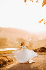 Fototapeta na wymiar Dreamy bride in a lush dress whirls near the lake at sunset