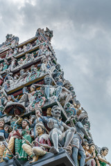 Fototapeta na wymiar Singapore - March 22, 2019: Sri Mariamman Hindu Temple on South Bridge Road. Closeup of detail of Gopuram tower shows plenty of colored statues with Dwarapalaka guardian up front.