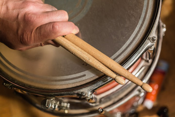 closeup detailed view of human person hands holding used drum sticks on old dusty snare drum...