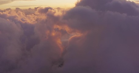 Aerial drone view flying above clouds at sunset, purple and gold clouds