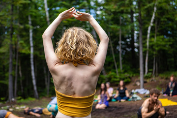 Diverse people enjoy spiritual gathering A young healthy and free spirited woman is seen practicing mindful dance amongst a group of people meditating during a multicultural celebration in nature.