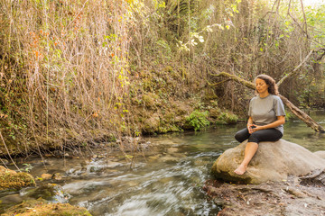 Meditating woman sitting on a rock at the edge of a river.