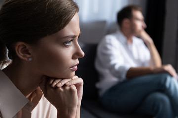 upset pensive young woman and husband sitting on sofa