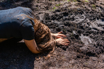 Diverse people enjoy spiritual gathering A closeup view of a young brunette woman, crouched over face down in a muddy puddle, seeking contemplation and enlightenment in nature during shamanic retreat.