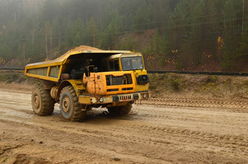 Big yellow dump truck working in the open-pit. Transporting sand and minerals. Mining quarry for the production of crushed stone, sand and gravel for use in the construction industry - image