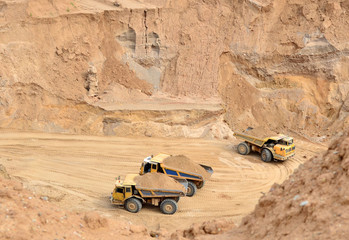 Big yellow dump trucks working in the open-pit. Transporting sand and minerals. Mining quarry for the production of crushed stone, sand and gravel for use in the construction industry - image