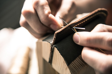 a tanner in a workshop makes a wallet from genuine leather in a special clip