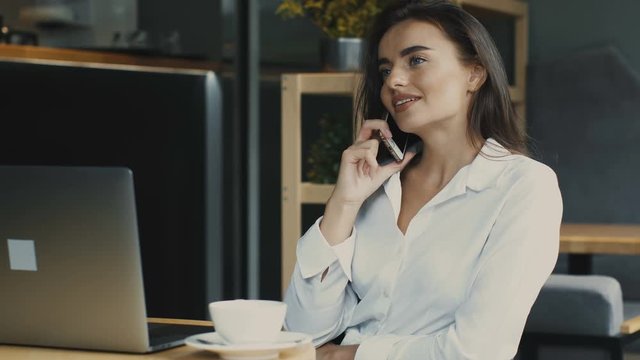 charming woman freelancer in cafe with laptop talking on phone and smiling