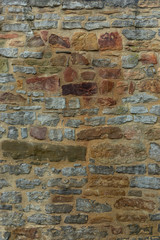 Natursteinmauer aus verschiedenen Natursteinen in verschiedenen Farben von dunkelgrau über gelb bis roten Sandstein