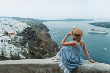 Travel Europe for summer holiday. Portrait of beautiful woman visitting old village Oia, Santorini island, Greece with sun hat and summer dress.