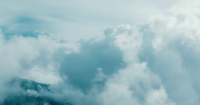 Aerial view flying in the midst of clouds in the sky with a mountain side in the background