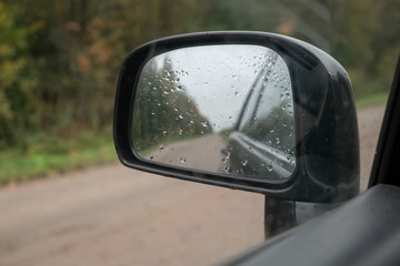 through a rearview mirror a dirt forest road is visible. Mirror covered with raindrops