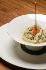 White turnip tagliatelle in a white bowl served on a wooden restaurant table. Exquisite dish. Creative restaurant meal. Fine dining concept.	