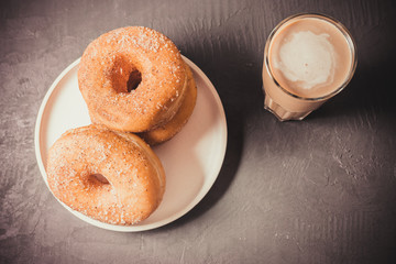 Coffee with milk and doughnuts on a dark table. Top view. Fresh pastries with coffee