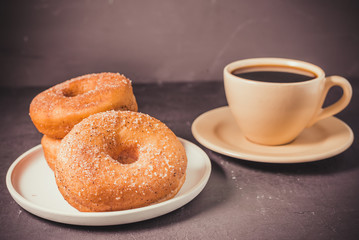 Doughnuts in a plate and a cup of black coffee. Selective focus. Dark background