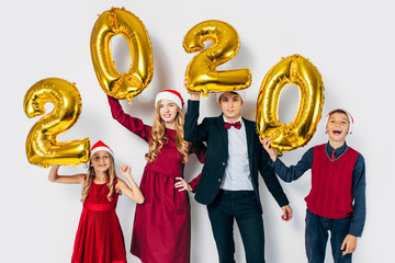 Young happy family with kids wearing Santa hats holding balloons shaped like numbers 2020 on white...