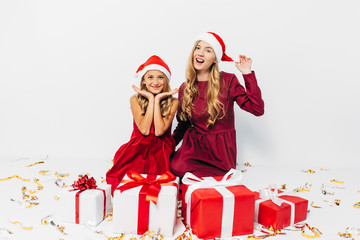 Young Christmas family, mom and daughter in Santa hats having fun with Christmas gifts, on white background.