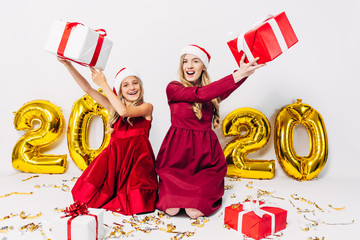 a happy mother and little daughter in Santa hats, having fun sitting on a white background with...