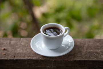 Black coffee in white cup on the edge of a village house balcony with natural background