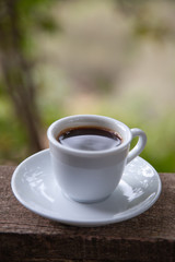Black coffee in white cup on the edge of a village house balcony with natural background