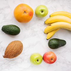 Fruits on a marble background. Bananas, apples, avocados, grapefruit, coconut. Copy space. Fruit frame.