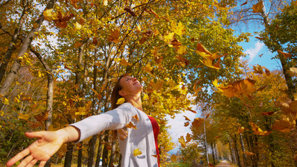 CLOSE UP: Woman outstretches her arms as the golden leaves fall from canopies