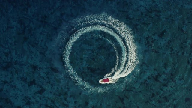 Slowmotion aerial shot of a fast speedboat with a red roof top driving around in the circle and making beautiful doughnuts in the clear turquoise magical sea. Top travel destination. 4K. 