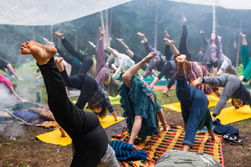 Diverse people enjoy spiritual gathering An intergenerational group of people wearing colorful clothes are seen practicing yoga in unison, all viewed with bare feet and one leg raised in the air.