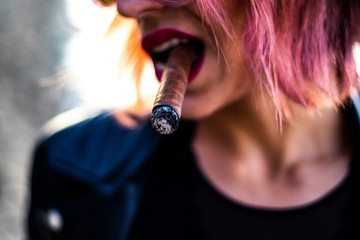 Extreme closeup on a cigar in the mouth of a woman with rebel and fashion style during the sunset,...